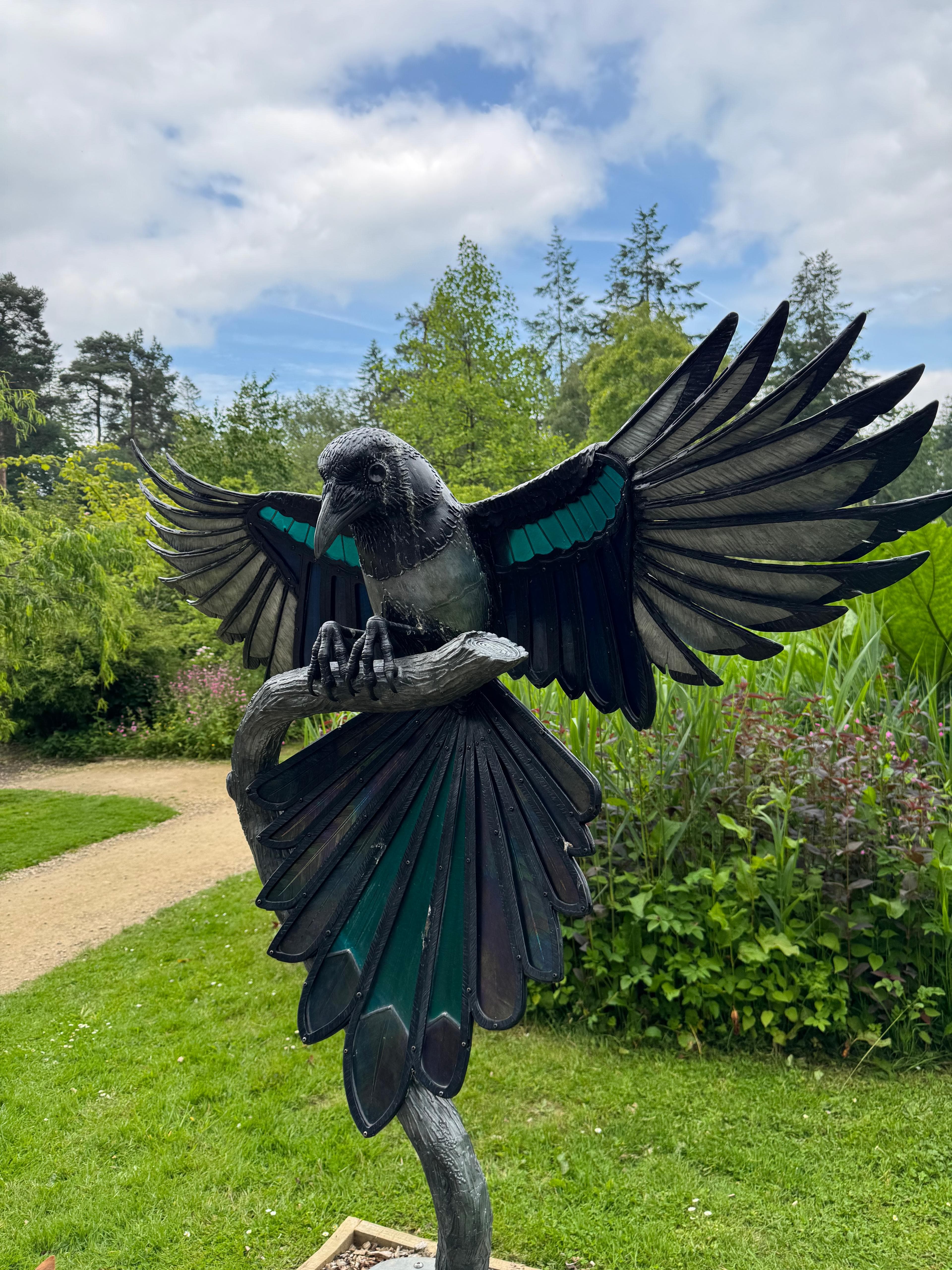 A detailed magpie sculpture with outstretched wings perched above the garden paths