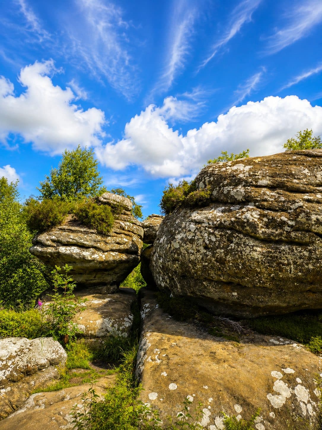 Balanced gritstone rocks at Brimham Rocks seen from below against a blue sky with wispy clouds