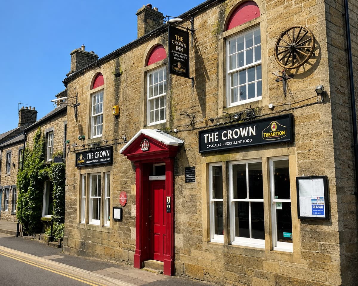 The stone exterior of The Crown Inn on Pateley Bridge High Street, with a red door and Theakston cask ales signage