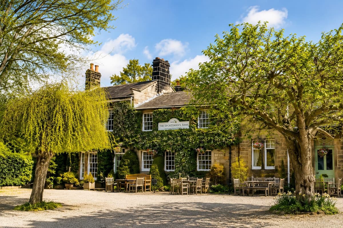 The ivy-covered stone exterior of the Sportsman's Arms at Wath, near Pateley Bridge, with a gravel courtyard, mature trees and outdoor seating