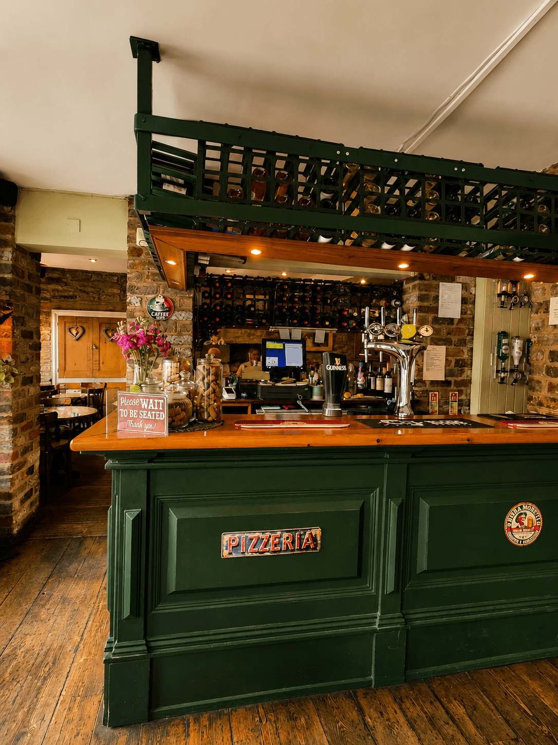 The dark green PIZZERIA bar counter inside Olley's Pizzeria in Pateley Bridge, with a Guinness tap and wine bottle racks above