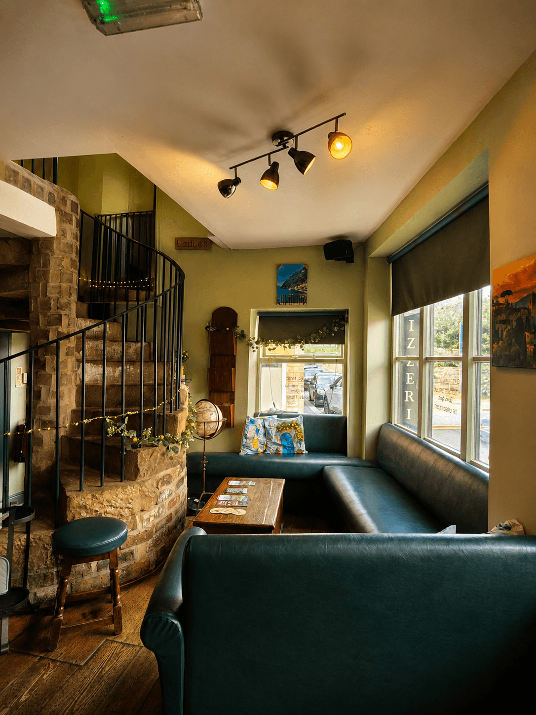A cosy green leather seating nook at Olley's Pizzeria, beside a stone spiral staircase up to further seating