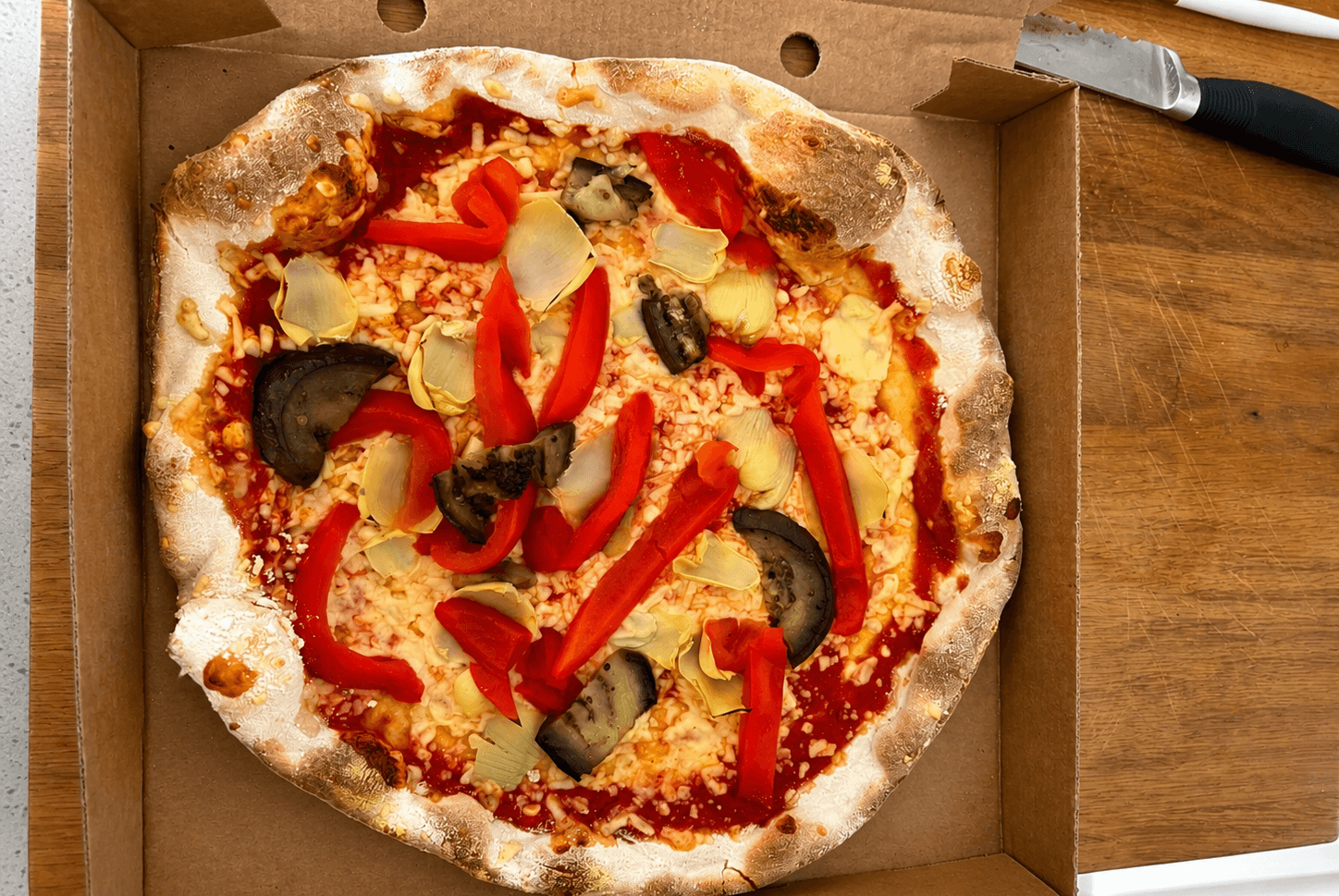 A wood-fired vegan pizza topped with roasted red peppers, artichoke and aubergine
